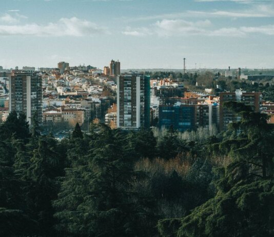 Aerial view of a city with high-rise buildings and lush trees in the foreground.