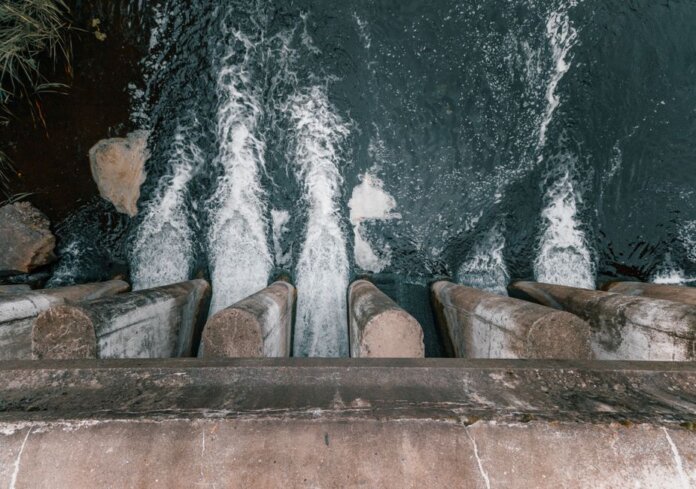 Aerial view of cascading water over a concrete dam showcasing turbulent flow and water management. Aerial view of cascading water over a concrete dam showcasing turbulent flow and water management.