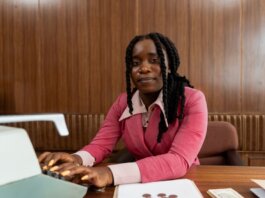African American woman in a pink suit typing on a retro typewriter in an office setting.