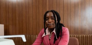 African American woman in a pink suit typing on a retro typewriter in an office setting.