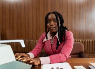 African American woman in a pink suit typing on a retro typewriter in an office setting.