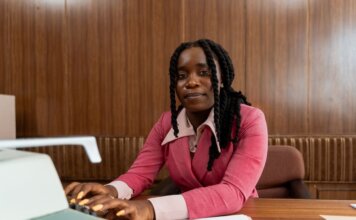 African American woman in a pink suit typing on a retro typewriter in an office setting.