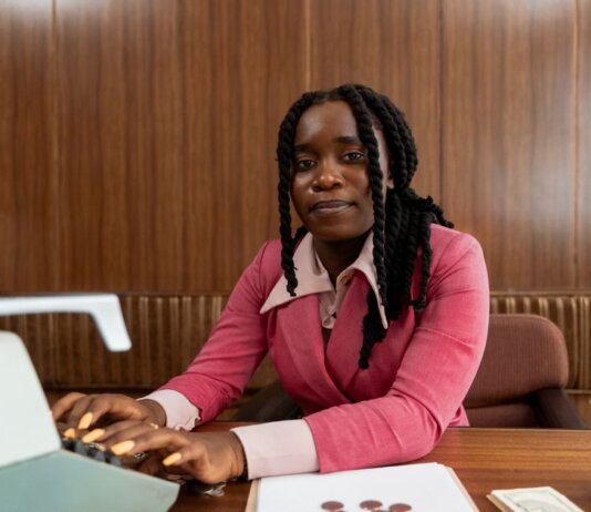 African American woman in a pink suit typing on a retro typewriter in an office setting.