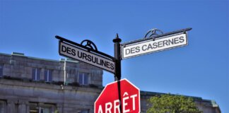 Bilingual street signs with stop sign against a clear blue sky in a city setting, featuring historical street names.