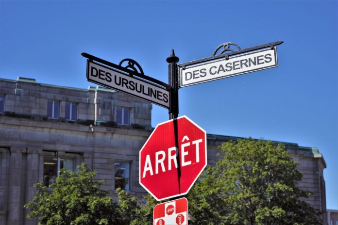 Bilingual street signs with stop sign against a clear blue sky in a city setting, featuring historical street names. Bilingual street signs with stop sign against a clear blue sky in a city setting, featuring historical street names.