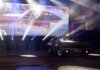 Classic muscle car illuminated by stage lights in a nostalgic indoor venue.