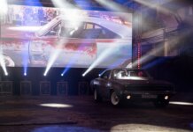 Classic muscle car illuminated by stage lights in a nostalgic indoor venue.