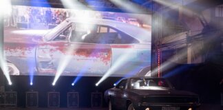 Classic muscle car illuminated by stage lights in a nostalgic indoor venue.
