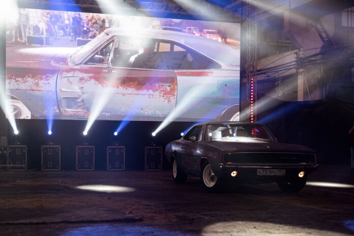 Classic muscle car illuminated by stage lights in a nostalgic indoor venue.