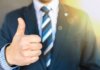 Close-up of a businessman in a suit giving a thumbs-up in a bright, positive setting.
