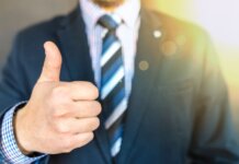 Close-up of a businessman in a suit giving a thumbs-up in a bright, positive setting.