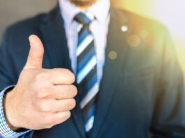 Close-up of a businessman in a suit giving a thumbs-up in a bright, positive setting.