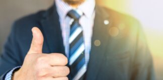 Close-up of a businessman in a suit giving a thumbs-up in a bright, positive setting.