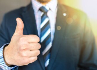 Close-up of a businessman in a suit giving a thumbs-up in a bright, positive setting.
