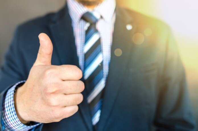 Close-up of a businessman in a suit giving a thumbs-up in a bright, positive setting. Close-up of a businessman in a suit giving a thumbs-up in a bright, positive setting.