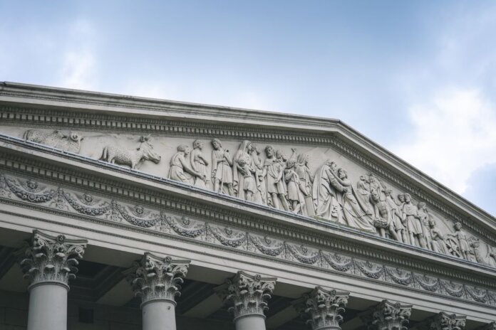 Close-up of a classical architectural pediment with detailed sculptures and columns. Close-up of a classical architectural pediment with detailed sculptures and columns.