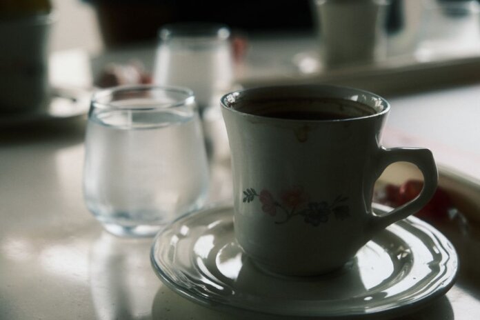 Close-up of a floral coffee cup and water glass on a table setting. Close-up of a floral coffee cup and water glass on a table setting.