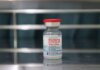 Close-up of a Moderna COVID-19 vaccine vial on a reflective metal surface.