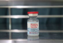 Close-up of a Moderna COVID-19 vaccine vial on a reflective metal surface.