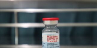 Close-up of a Moderna COVID-19 vaccine vial on a reflective metal surface.