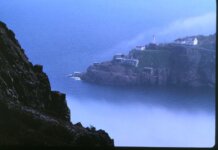 Dramatic coastal view of St. John's harbor with lighthouse amidst fog.