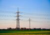 Dusk landscape showing transmission towers and lush fields under a clear sky.