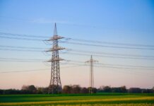Dusk landscape showing transmission towers and lush fields under a clear sky.