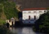 Eguzon hydroelectric plant by a river during sunset, surrounded by lush greenery.