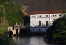 Eguzon hydroelectric plant by a river during sunset, surrounded by lush greenery.