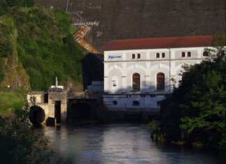 Eguzon hydroelectric plant by a river during sunset, surrounded by lush greenery.