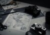 Electronic devices for taking photo and scissors with pencil composing with herbarium and detailed map of world on table in room