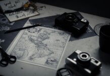 Electronic devices for taking photo and scissors with pencil composing with herbarium and detailed map of world on table in room