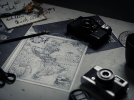 Electronic devices for taking photo and scissors with pencil composing with herbarium and detailed map of world on table in room