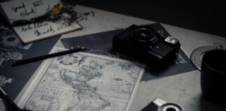 Electronic devices for taking photo and scissors with pencil composing with herbarium and detailed map of world on table in room