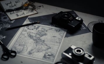 Electronic devices for taking photo and scissors with pencil composing with herbarium and detailed map of world on table in room