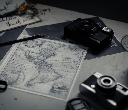 Electronic devices for taking photo and scissors with pencil composing with herbarium and detailed map of world on table in room
