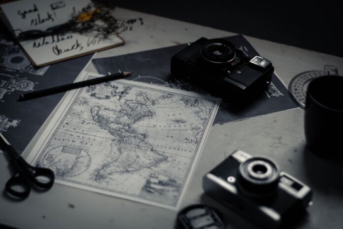 Electronic devices for taking photo and scissors with pencil composing with herbarium and detailed map of world on table in room
