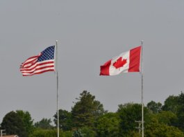 Flags of the USA and Canada waving on flagpoles against a clear sky in Sarnia, Ontario.