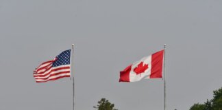 Flags of the USA and Canada waving on flagpoles against a clear sky in Sarnia, Ontario.