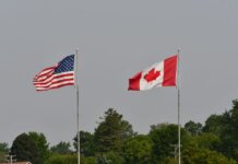 Flags of the USA and Canada waving on flagpoles against a clear sky in Sarnia, Ontario.