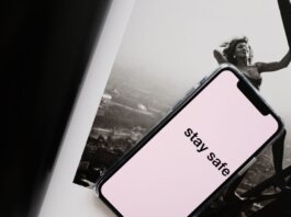 From above of cellphone with pale pink screen and STAY SAFE inscription put on open magazine with image of cheerful female climbing metal tower