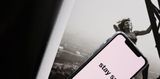 From above of cellphone with pale pink screen and STAY SAFE inscription put on open magazine with image of cheerful female climbing metal tower