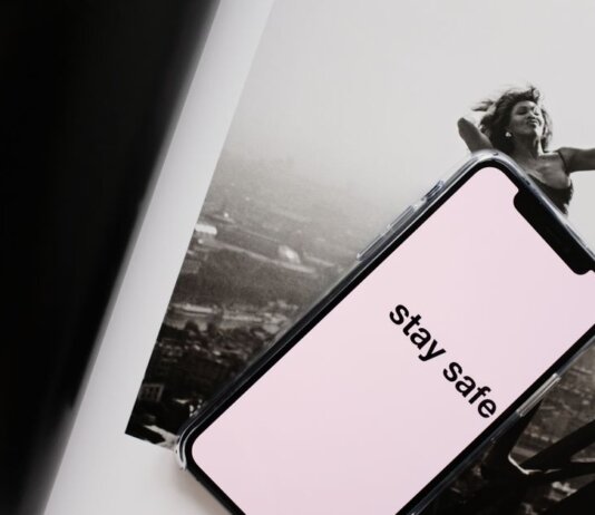 From above of cellphone with pale pink screen and STAY SAFE inscription put on open magazine with image of cheerful female climbing metal tower