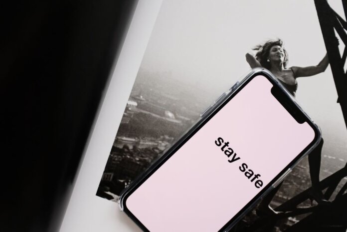 From above of cellphone with pale pink screen and STAY SAFE inscription put on open magazine with image of cheerful female climbing metal tower From above of cellphone with pale pink screen and STAY SAFE inscription put on open magazine with image of cheerful female climbing metal tower