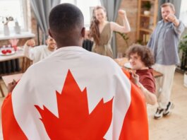 Group of friends celebrating Canada Day indoors with a Canadian flag draped over one person.