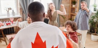Group of friends celebrating Canada Day indoors with a Canadian flag draped over one person.