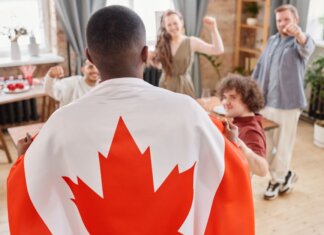 Group of friends celebrating Canada Day indoors with a Canadian flag draped over one person.