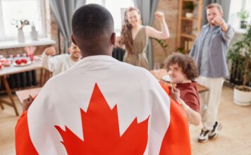 Group of friends celebrating Canada Day indoors with a Canadian flag draped over one person.