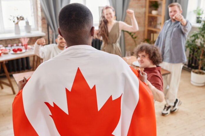 Group of friends celebrating Canada Day indoors with a Canadian flag draped over one person. Group of friends celebrating Canada Day indoors with a Canadian flag draped over one person.