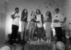 Group of friends celebrating indoors with confetti and balloons in a black and white setting.